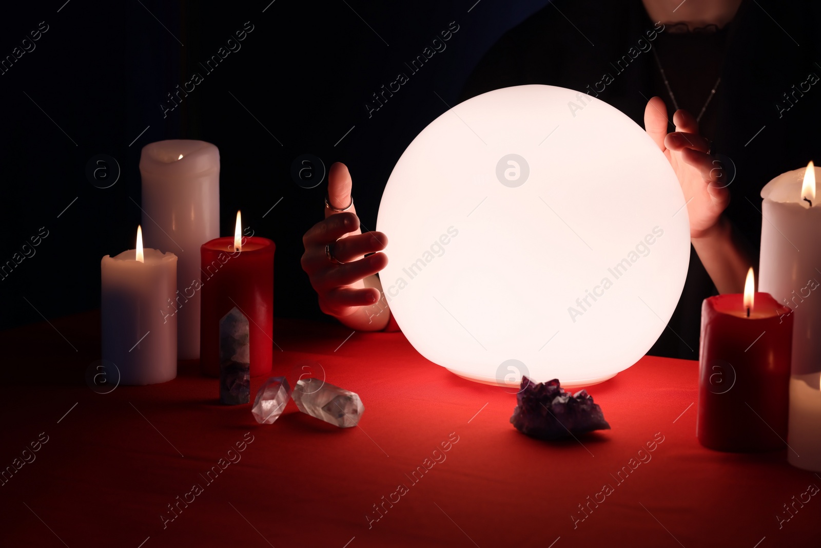 Photo of Soothsayer using glowing crystal ball to predict future  at table in darkness, closeup. Fortune telling