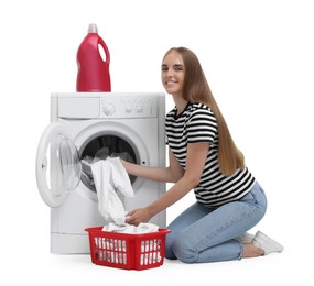 Beautiful young woman taking laundry out of washing machine on white background