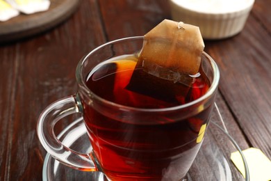 Photo of Brewing tea. Glass cup with tea bag on wooden table, closeup