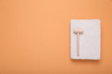 Photo of Educational toy for motor skills development. Excavation kit (plaster and wooden mallet) on orange background, top view with space for text