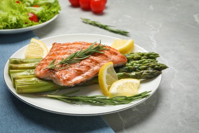 Tasty grilled salmon with asparagus, lemon and rosemary on light grey table