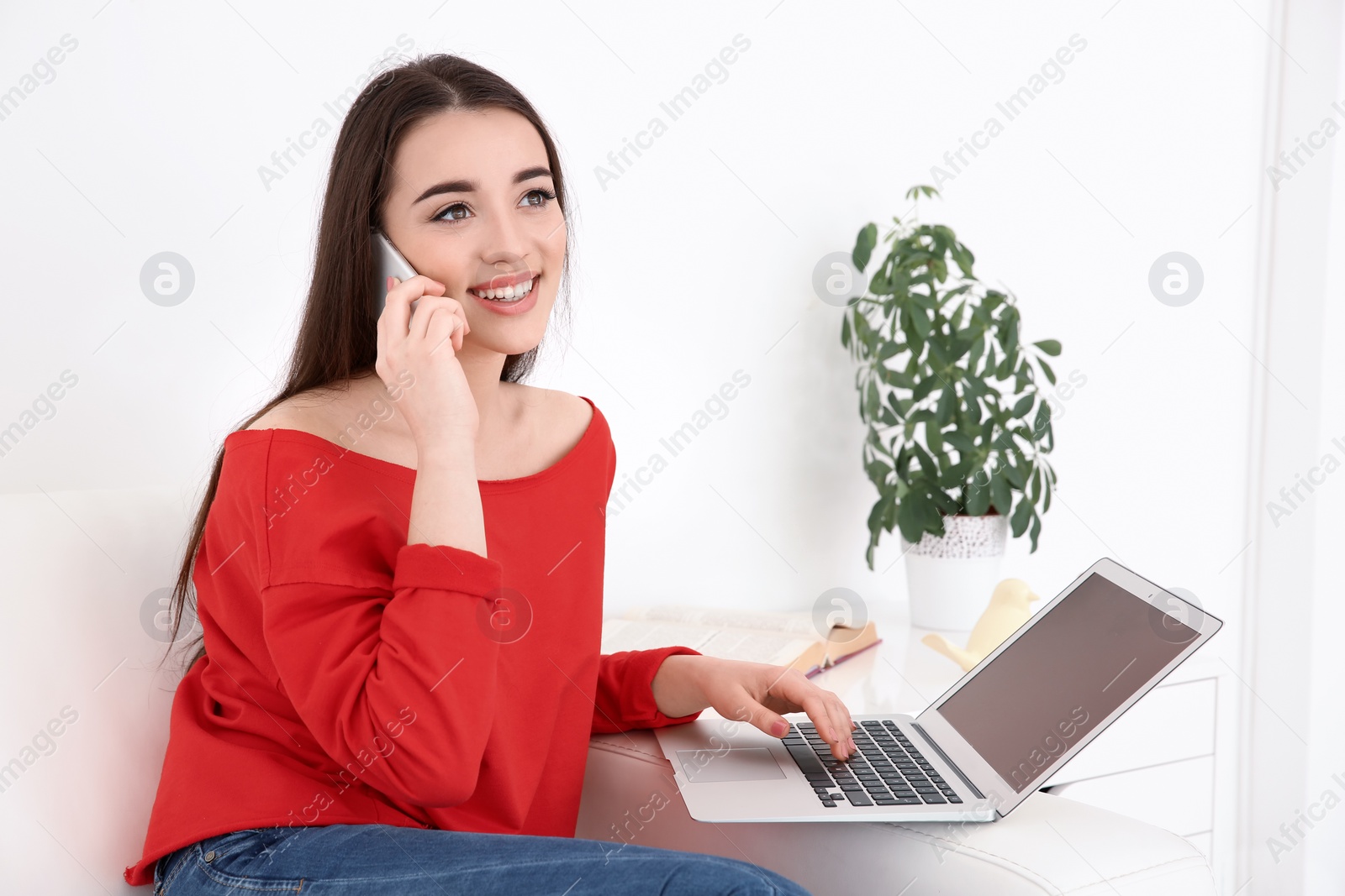 Photo of Attractive young woman talking on mobile phone while using laptop at home