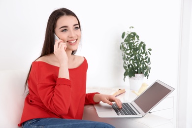 Photo of Attractive young woman talking on mobile phone while using laptop at home