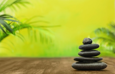 Photo of Table with stack of stones and blurred green leaves on background, space for text. Zen concept