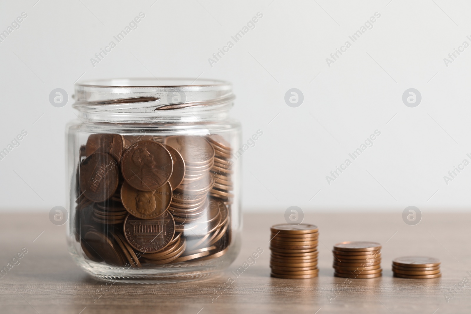 Photo of Glass jar with money and stack of coins on wooden table, closeup