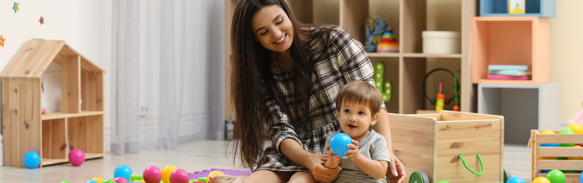 Image of Young nanny and cute little baby playing with toys at home. Banner design 