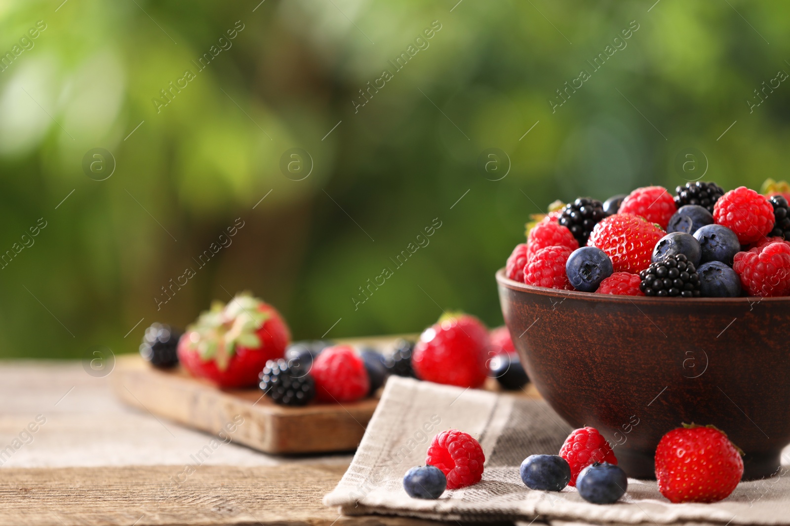Photo of Bowl and different fresh ripe berries on wooden table outdoors, space for text