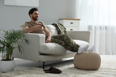 Photo of Happy soldier watching TV on sofa in living room. Military service