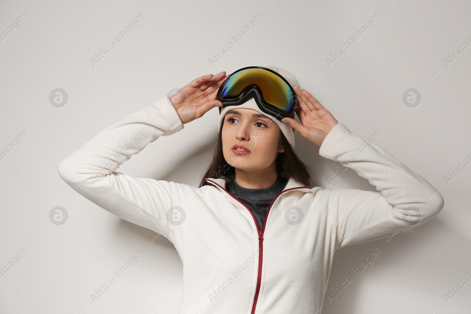 Photo of Woman wearing fleece jacket and goggles on light grey background. Winter sport clothes