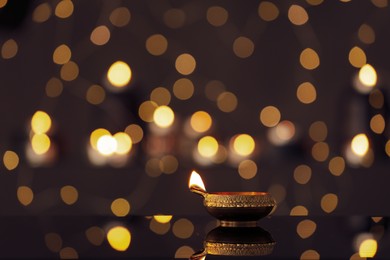 Photo of Lit diya on table against blurred lights, space for text. Diwali lamp