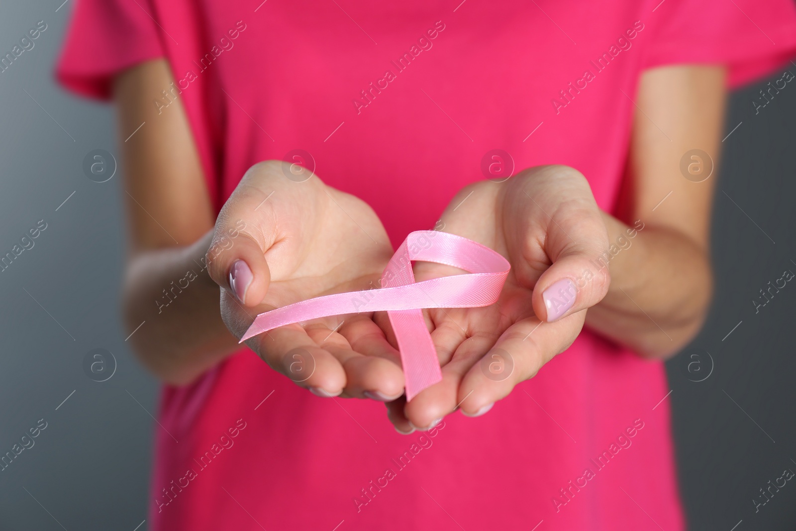 Photo of Woman holding pink ribbon on grey background, closeup. Breast cancer awareness