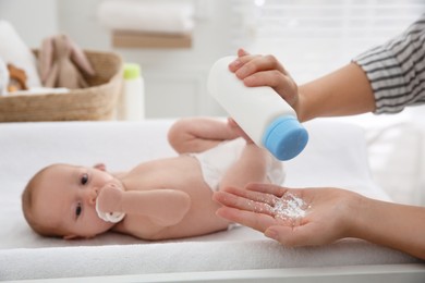 Mother with bottle of dusting powder near her cute baby at home