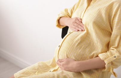 Photo of Beautiful pregnant woman sitting in light room, closeup