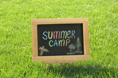 Photo of Blackboard with text SUMMER CAMP and drawings on green grass