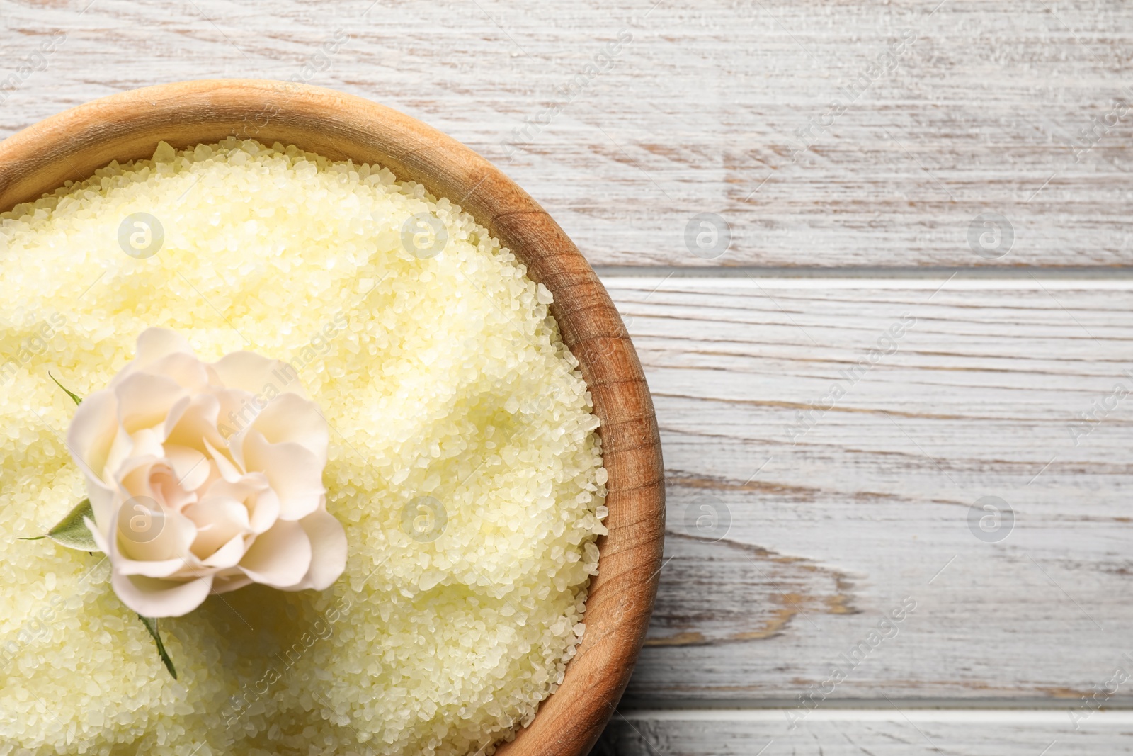 Photo of Yellow sea salt on white wooden table, top view. Space for text