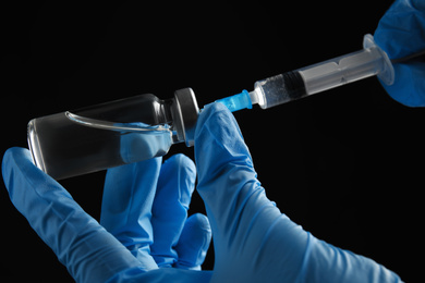 Photo of Doctor filling syringe with medication on black background, closeup. Vaccination and immunization