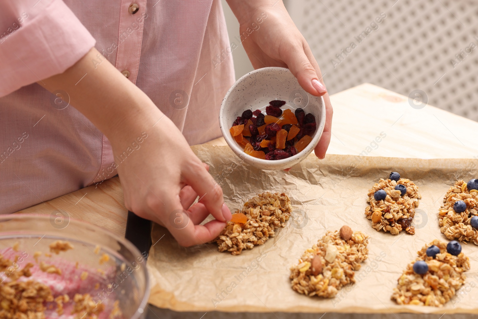 Photo of Making granola bars. Woman with dry fruits at table in kitchen, closeup