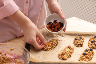 Making granola bars. Woman with dry fruits at table in kitchen, closeup