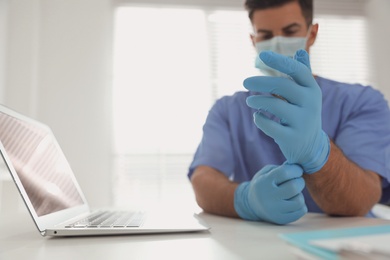 Photo of Doctor in medical gloves at table in office, focus on hands