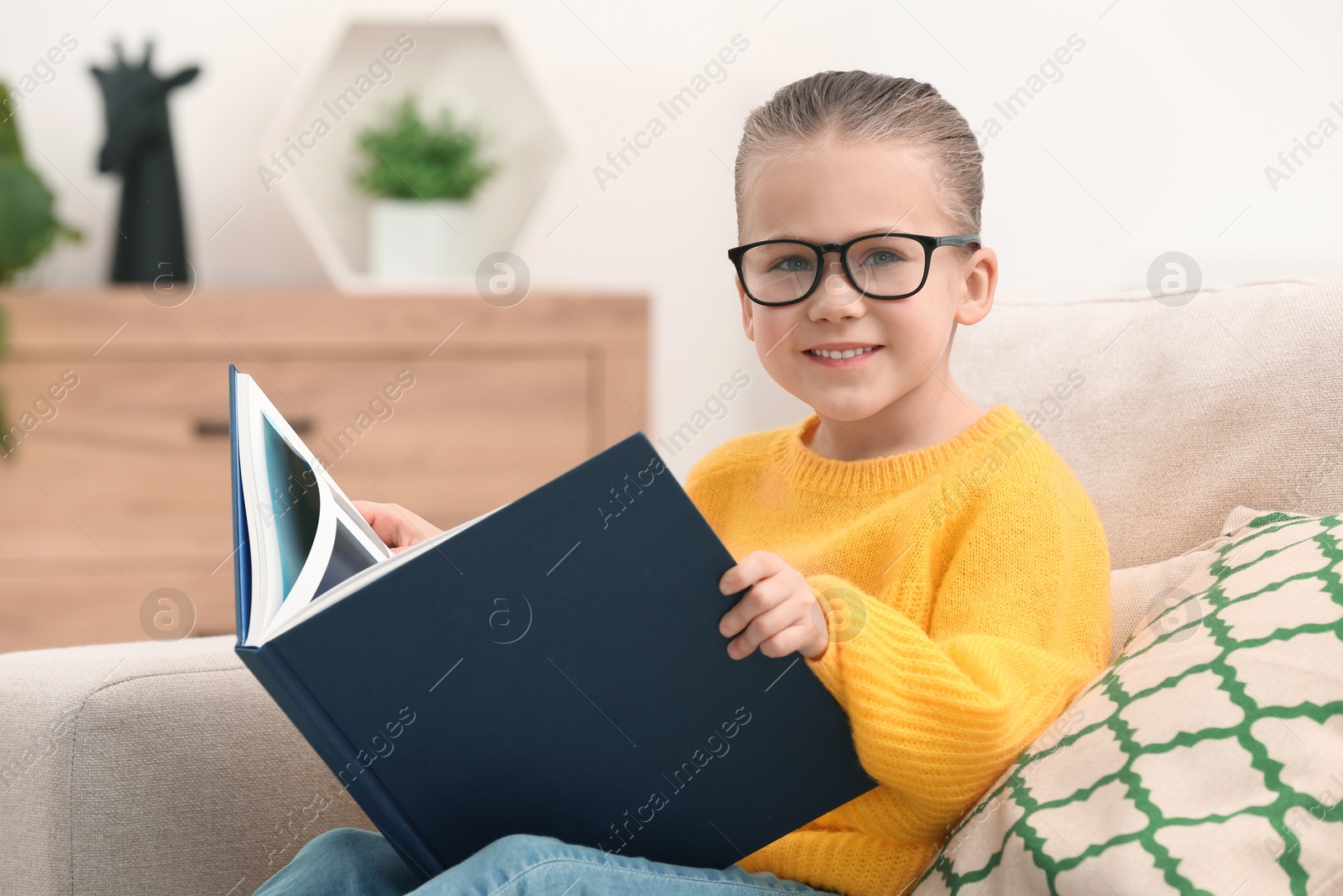 Photo of Portrait of cute little girl in glasses with book indoors