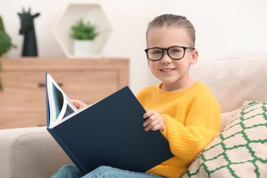 Photo of Portrait of cute little girl in glasses with book indoors