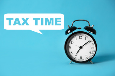 Image of Time to pay taxes. Alarm clock on light blue background
