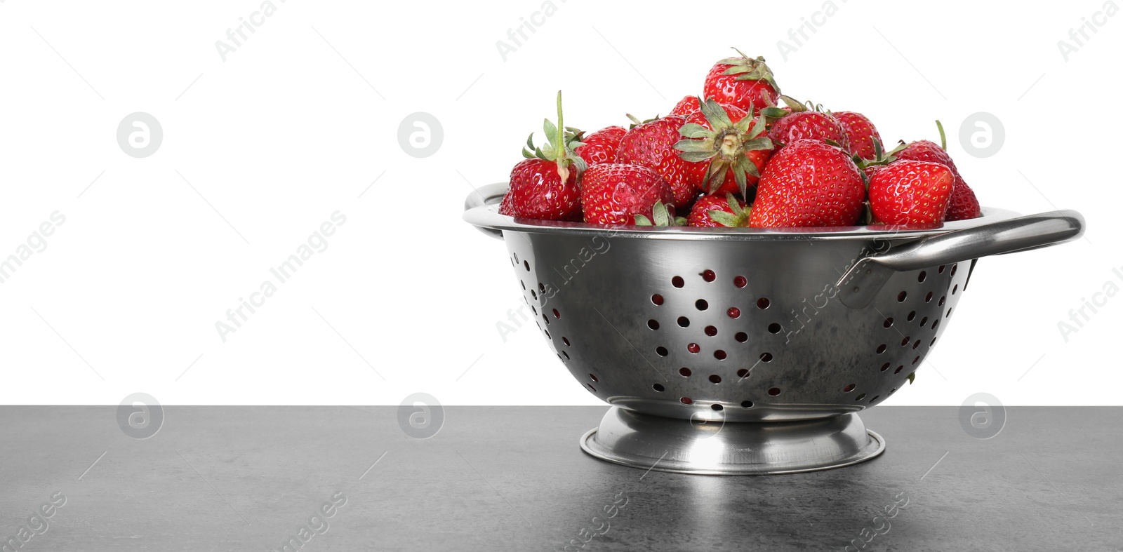 Photo of Metal colander with fresh strawberries on grey table against white background. Space for text