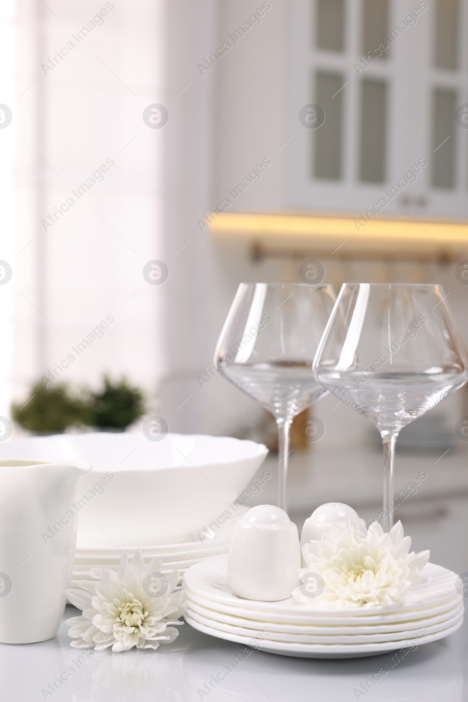 Photo of Set of clean dishware, glasses and flowers on table in kitchen, space for text