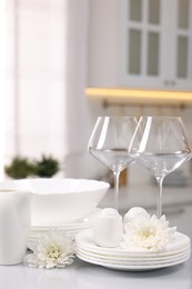 Photo of Set of clean dishware, glasses and flowers on table in kitchen, space for text