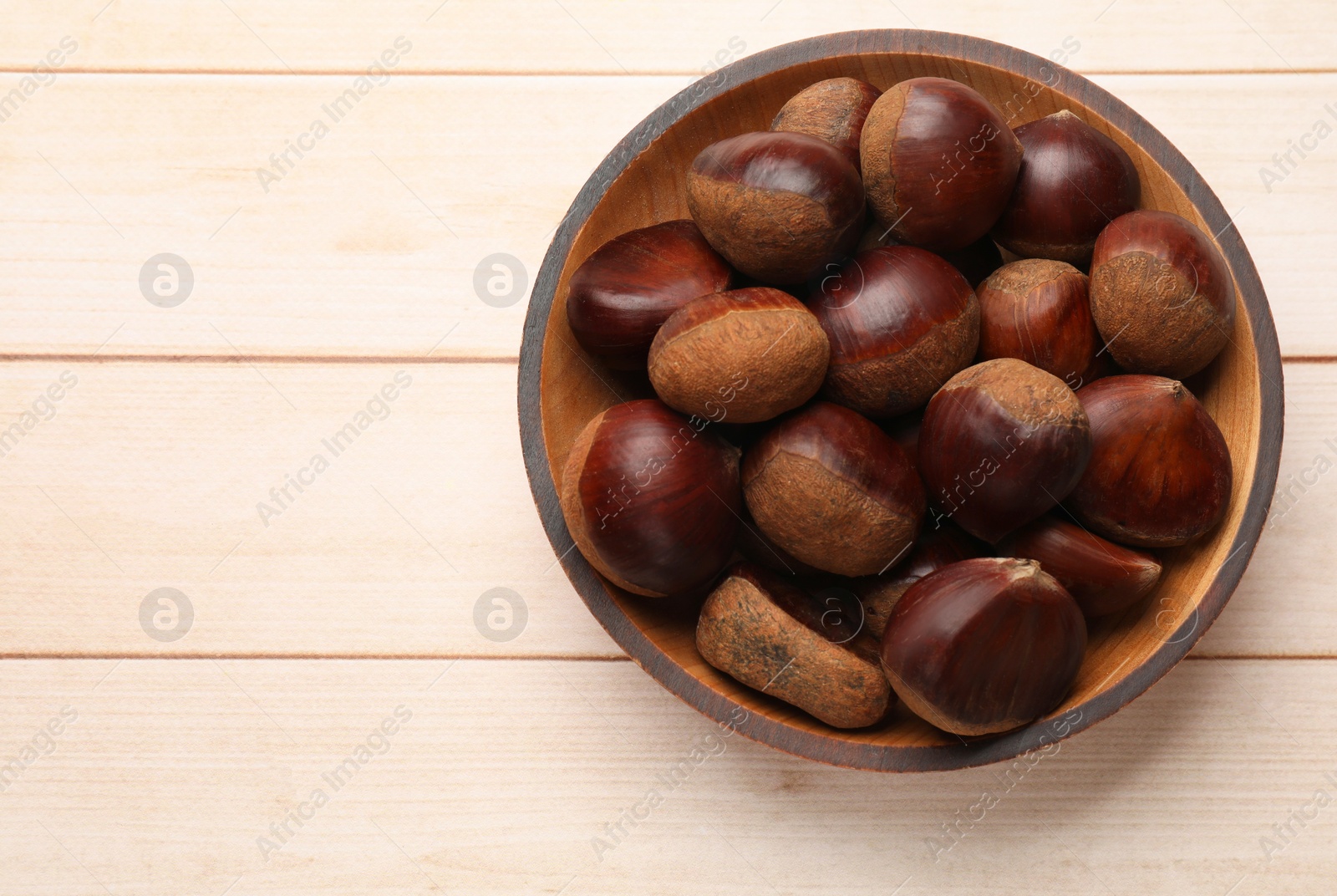 Photo of Sweet fresh edible chestnuts on light wooden table, top view. Space for text