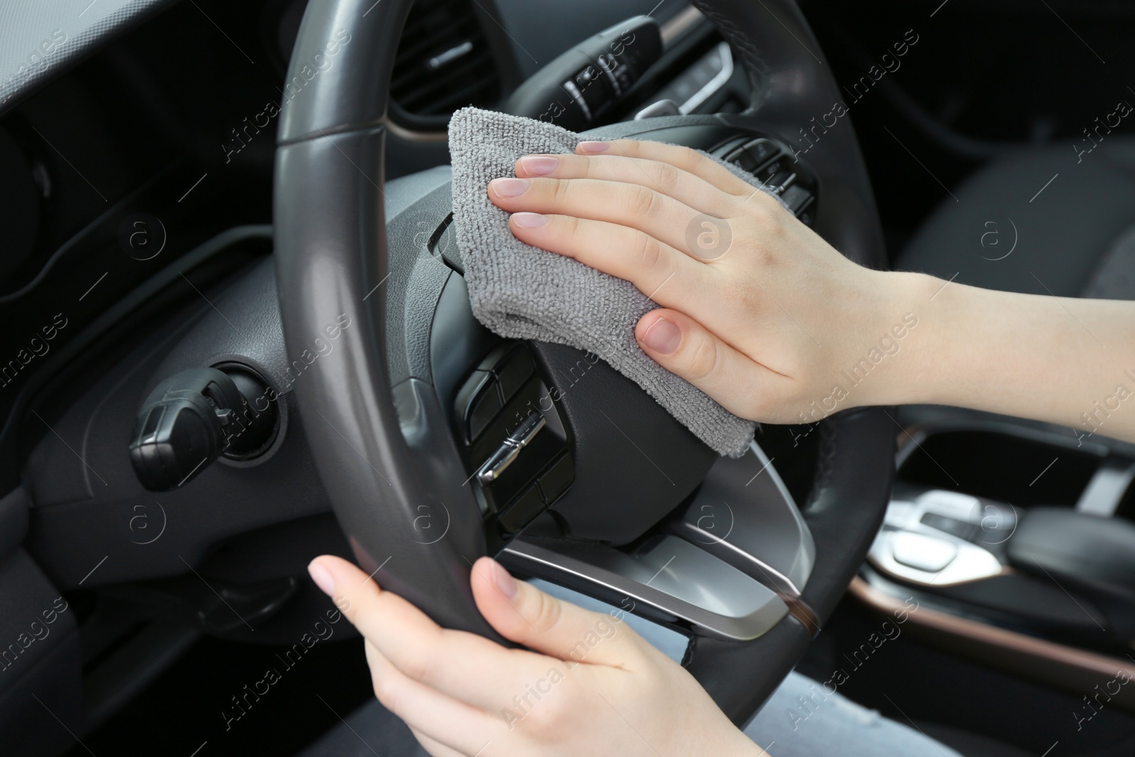 Photo of Woman cleaning steering wheel with rag in car, closeup