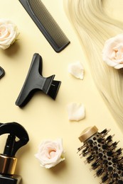 Photo of Flat lay composition with different hairdresser tools and flowers on pale yellow background