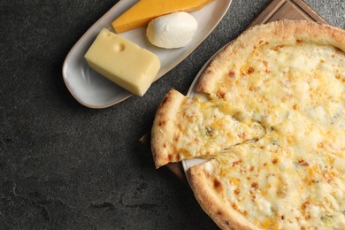 Delicious cheese pizza and different kinds of cheese on dark grey table, flat lay. Space for text