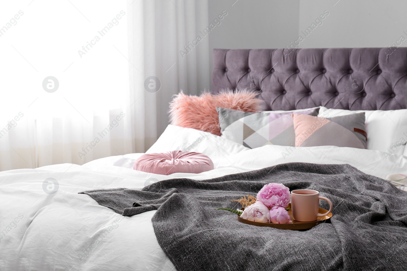 Photo of Cup of drink and bouquet on bed with pillows in room