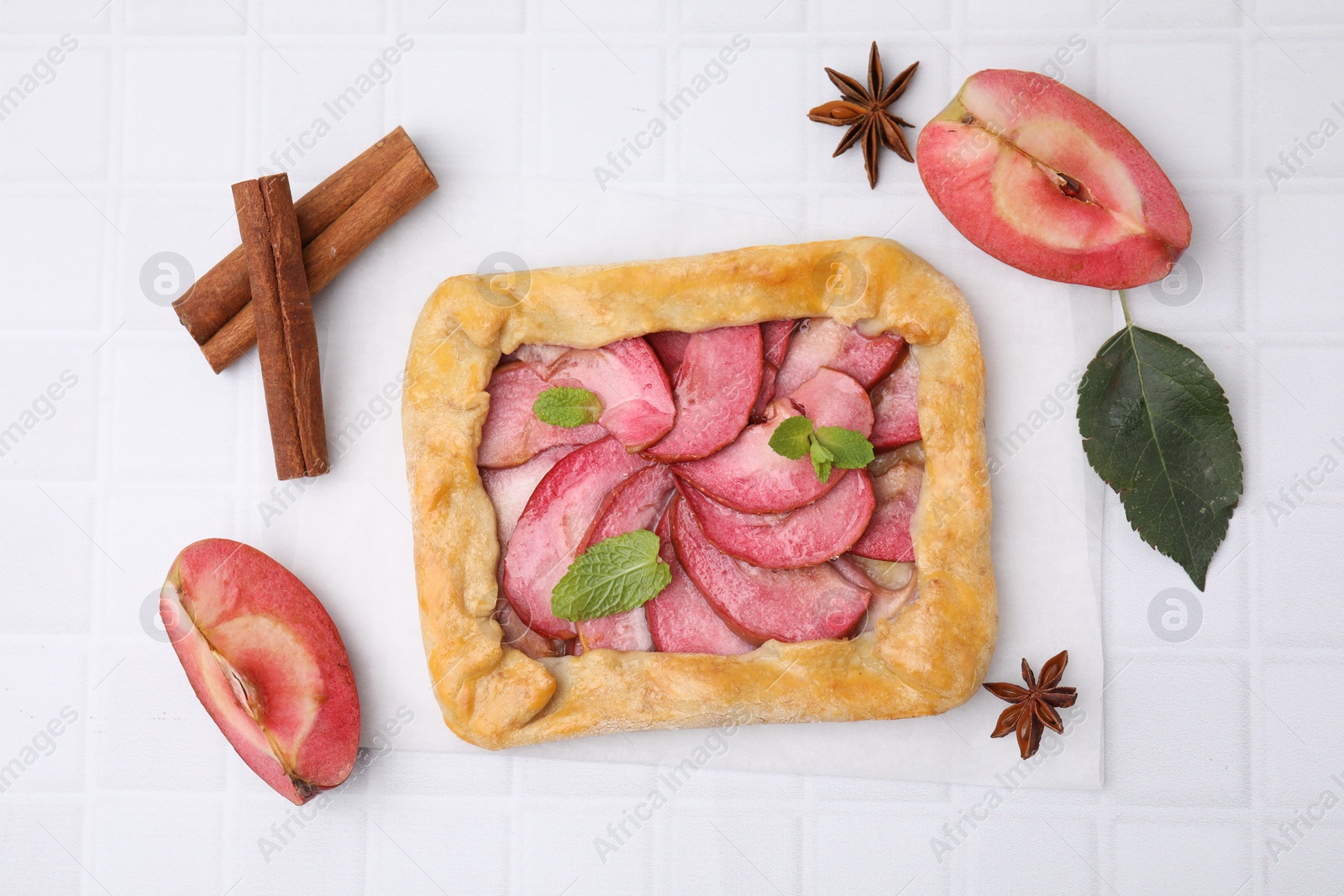 Photo of Delicious apple galette with mint and ingredients on white tiled table, flat lay