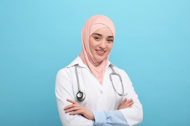 Muslim woman wearing hijab and medical uniform with stethoscope on light blue background