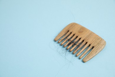 Photo of Wooden comb with lost hair on light blue background. Space for text