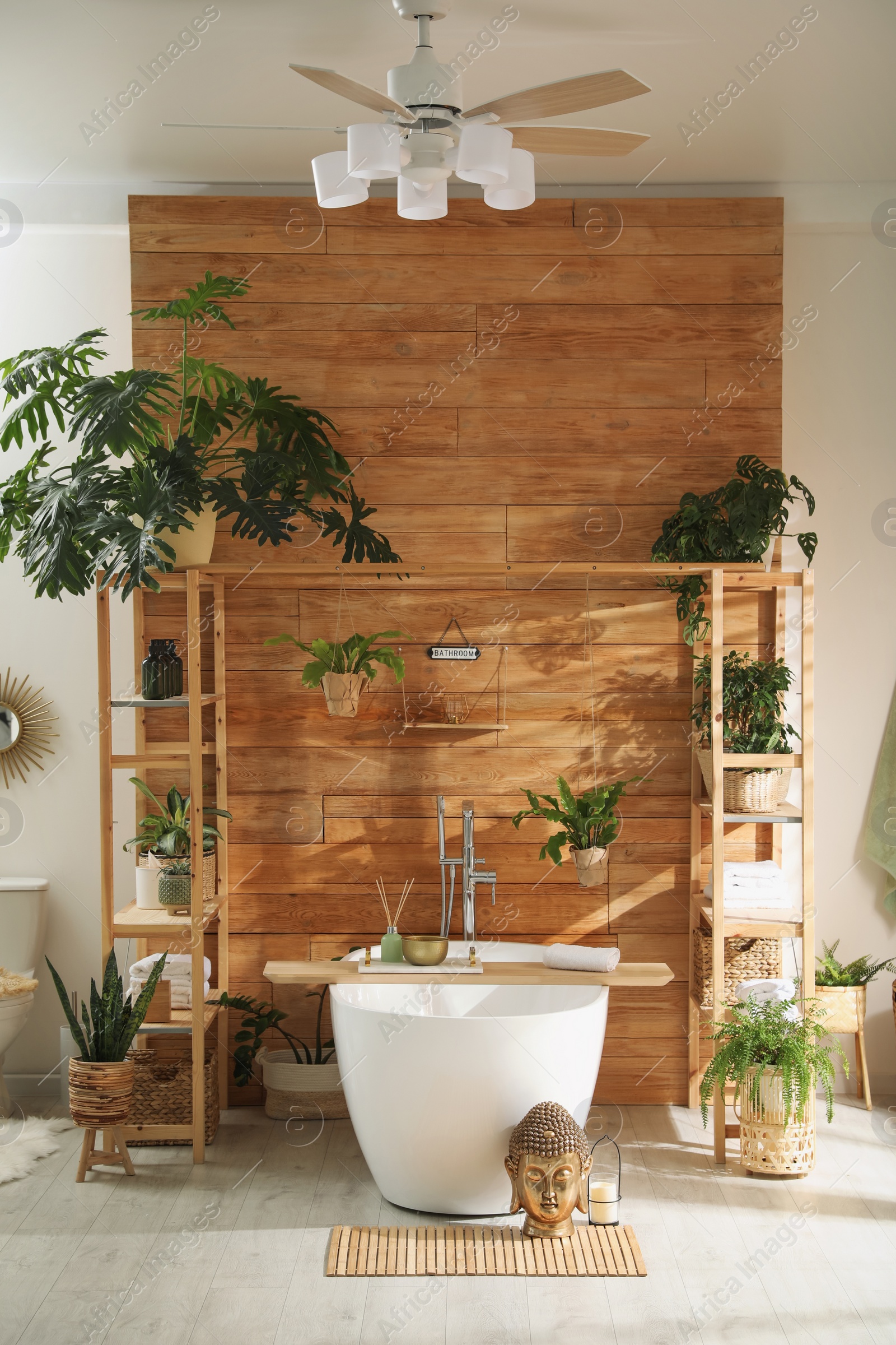 Photo of Stylish bathroom interior with white tub and green houseplants near wooden wall. Idea for design