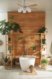 Stylish bathroom interior with white tub and green houseplants near wooden wall. Idea for design