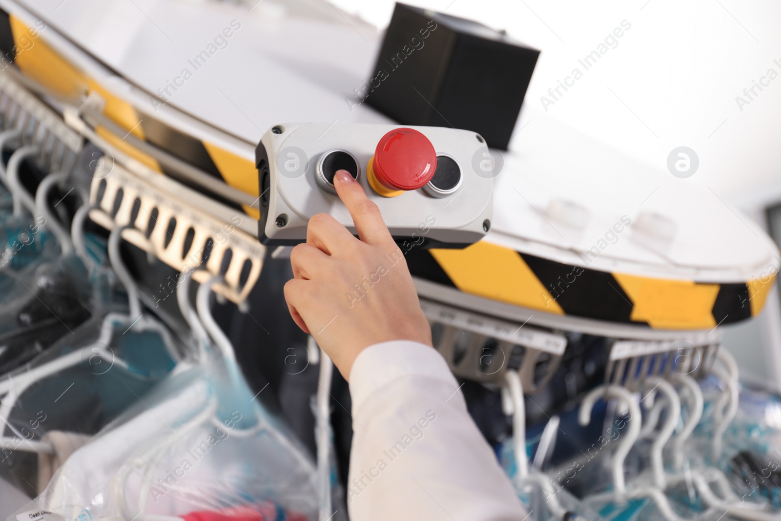 Photo of Worker pressing button on control panel of garment conveyor at modern dry-cleaner's, closeup