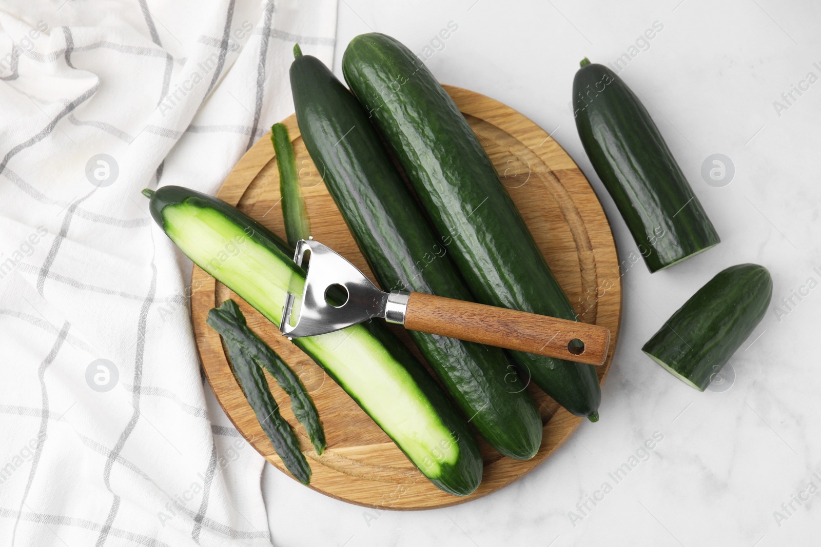 Photo of Fresh cucumbers and peeler on white marble table, top view