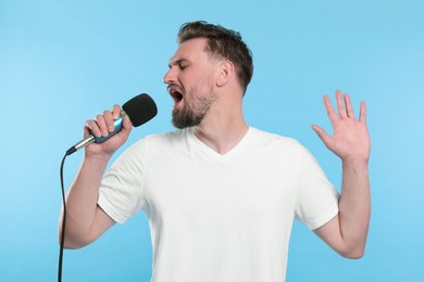 Photo of Handsome man with microphone singing on light blue background