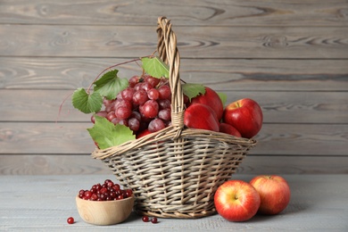 Photo of Wicker basket with fresh fruits and berries on grey wooden table