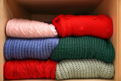 Different folded warm sweaters on wooden shelf