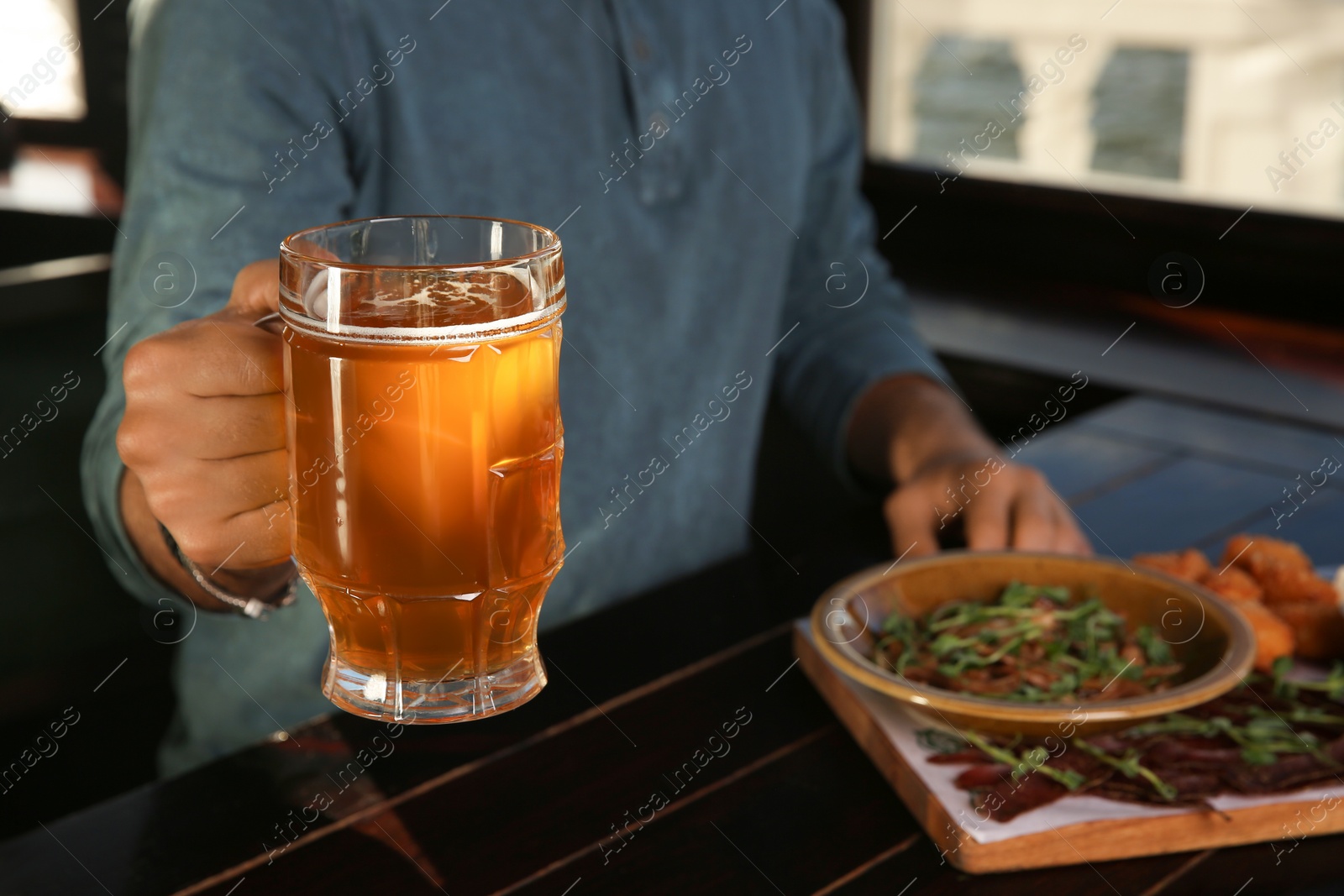 Photo of Man with glass of tasty beer at wooden table in pub, closeup. Space for text