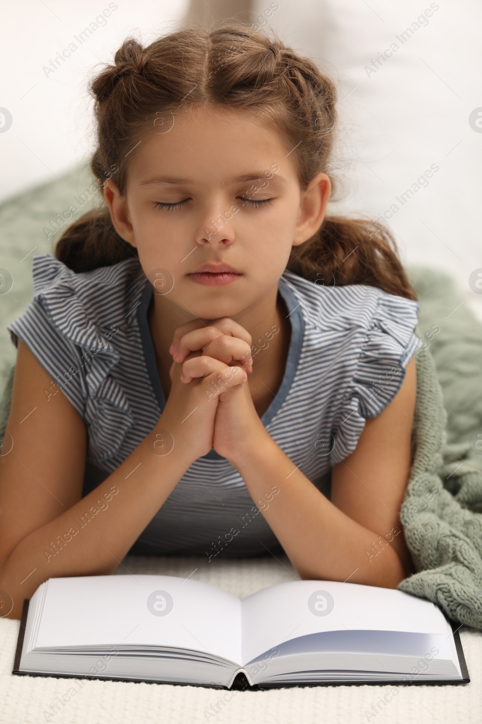 Photo of Cute little girl praying over Bible in bedroom