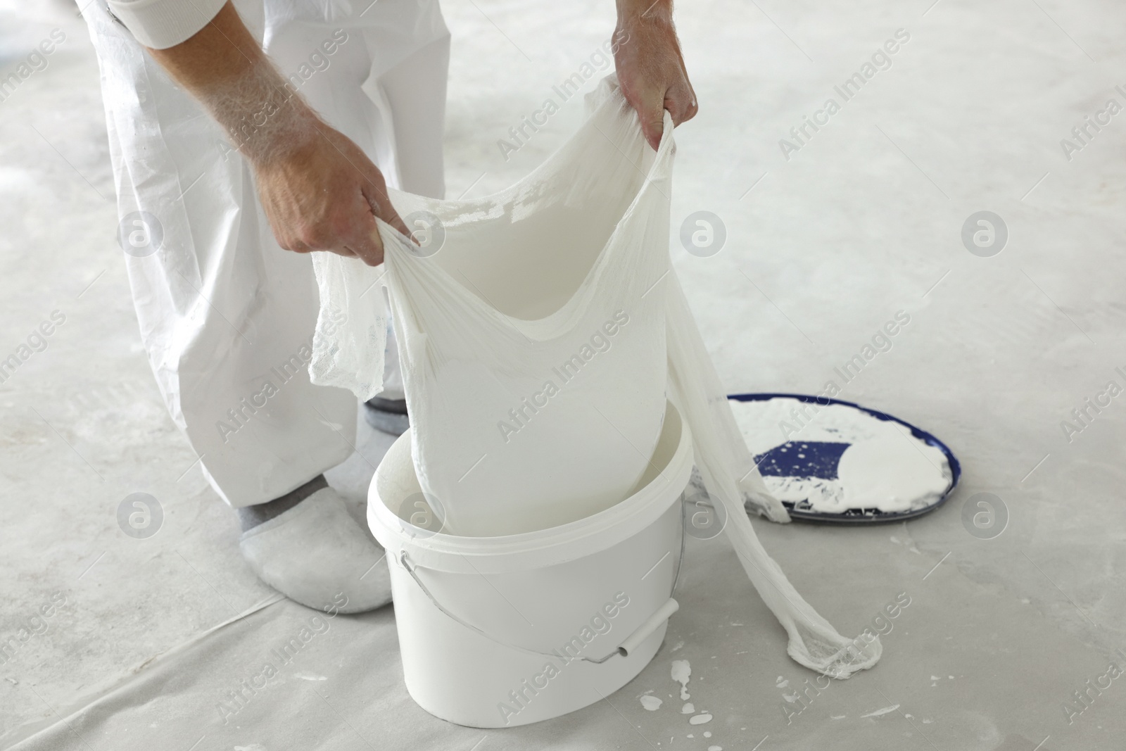 Photo of Decorator filtering paint in bucket on white floor, closeup