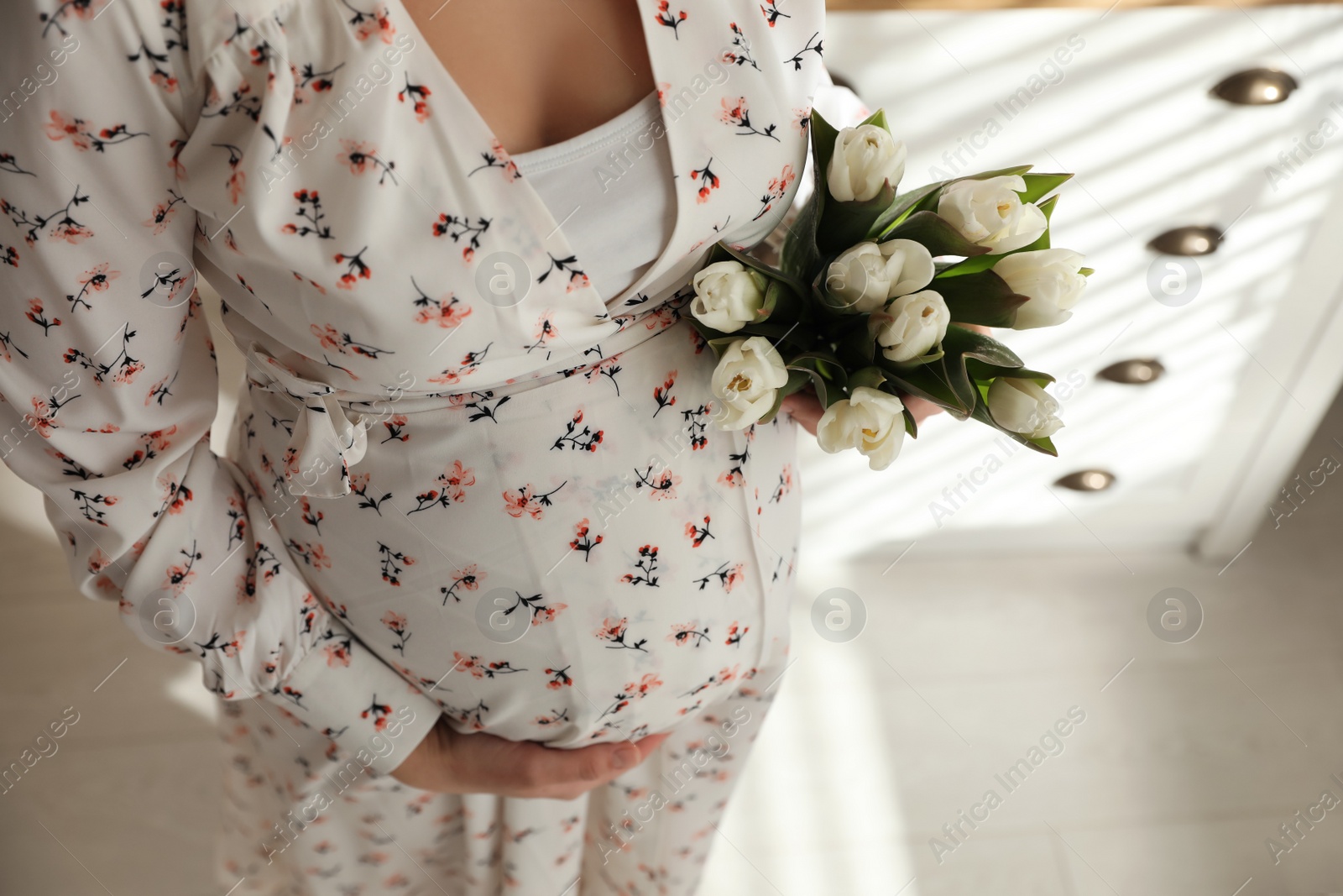 Photo of Young pregnant woman with flowers indoors, closeup