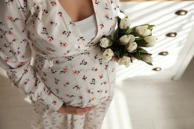 Young pregnant woman with flowers indoors, closeup