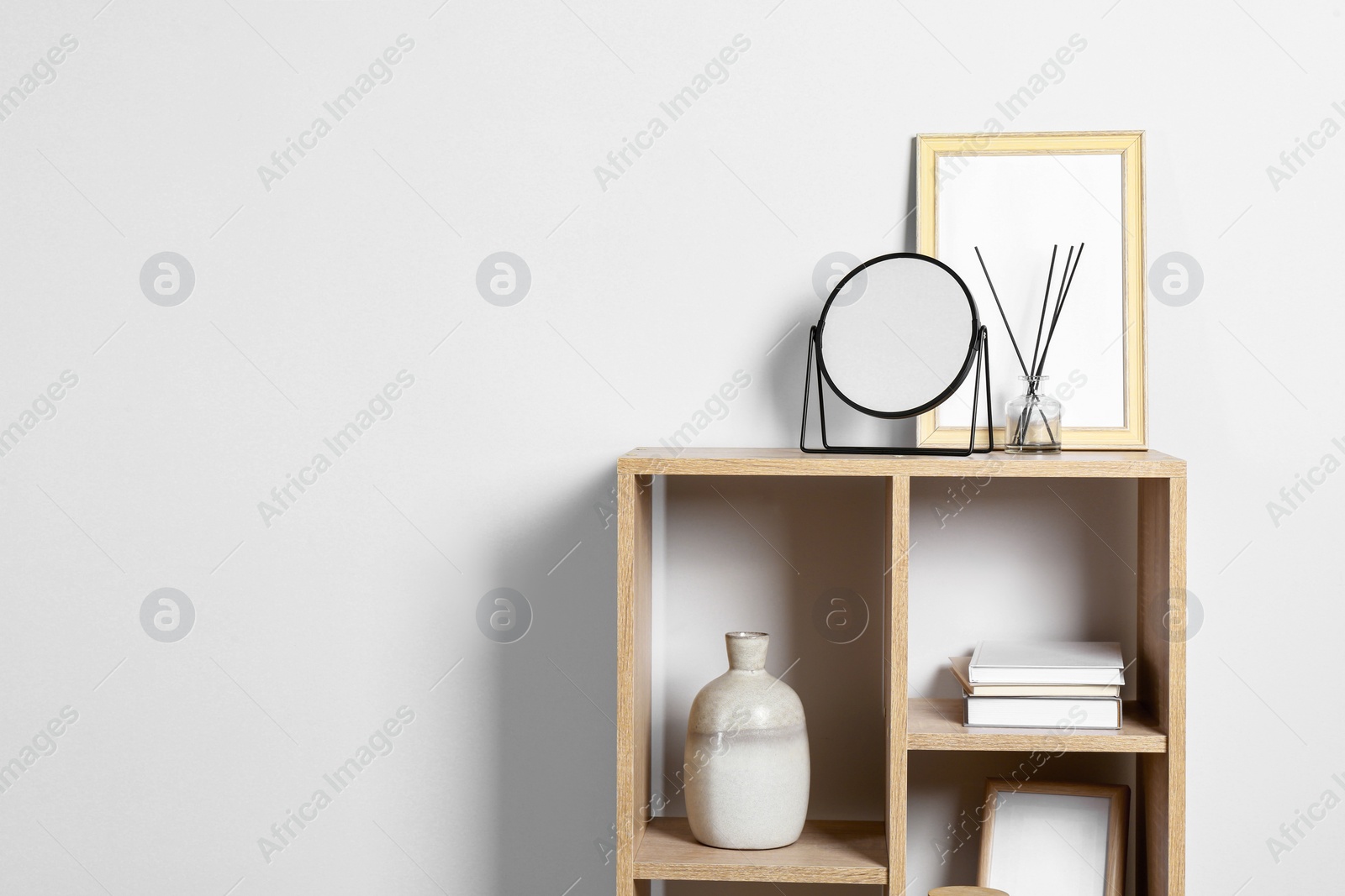 Photo of Stylish mirror, reed diffuser and picture frame on shelf near light wall, space for text. Interior design